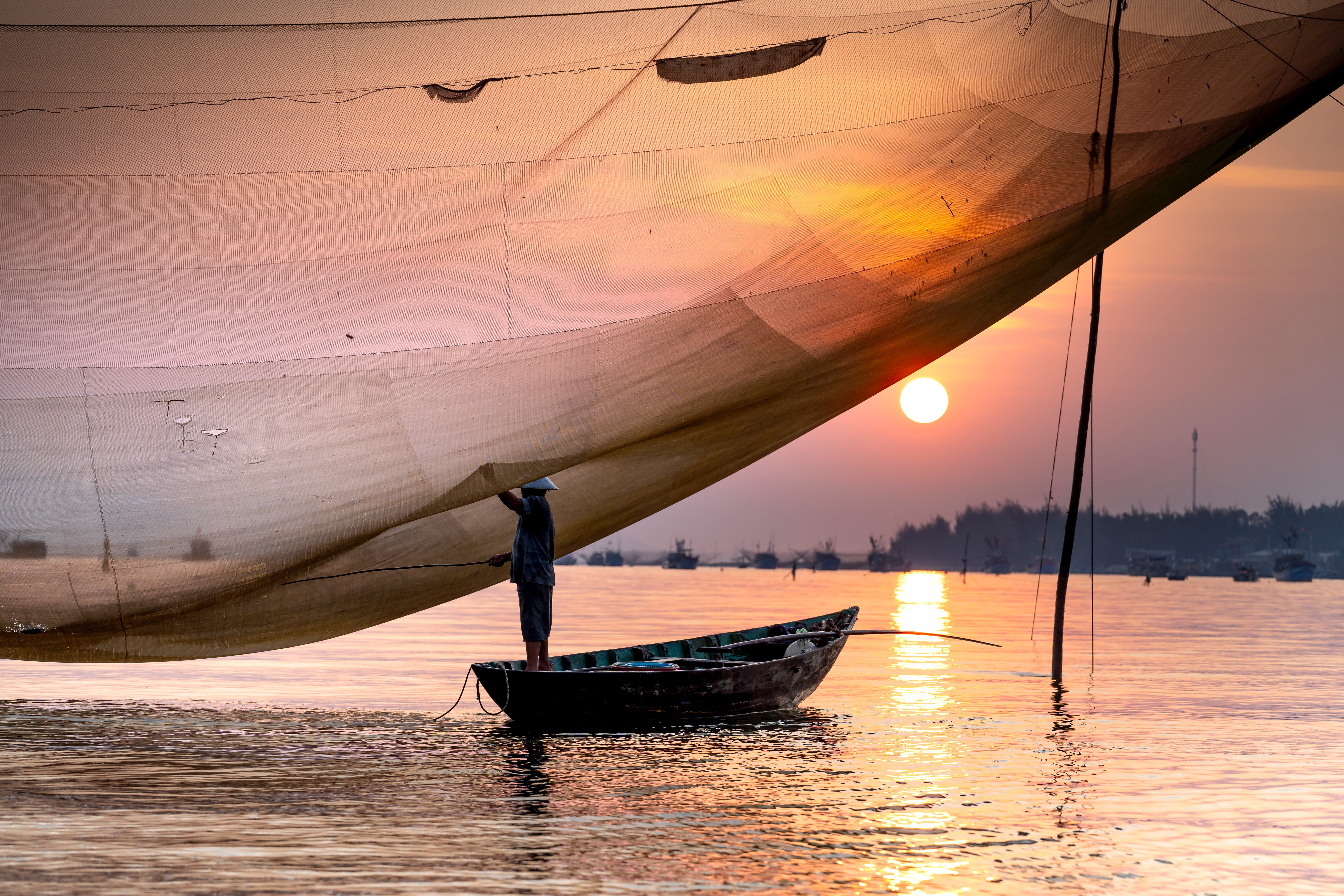 A photo of a fisher under a wide net on the water as the sun sets