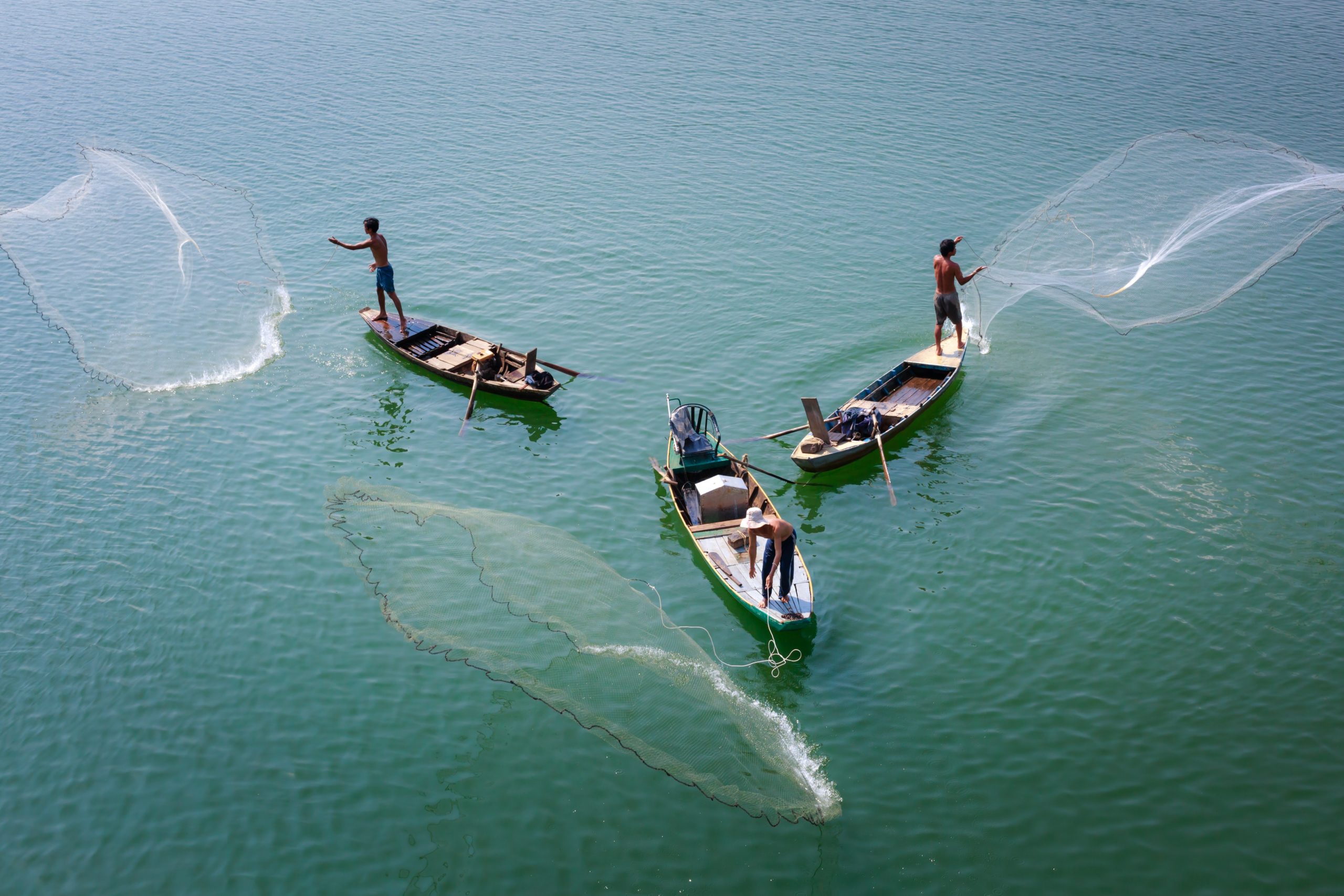 Three fishers casting nets off the side of their boats