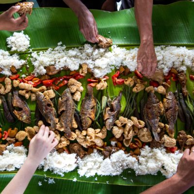 People share fried fish and rice served on a giant banana leaf.