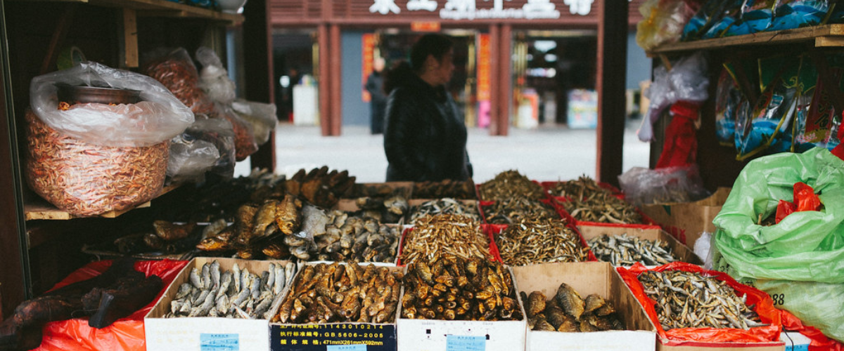 Woman stands behind market of dried fish in boxes.
