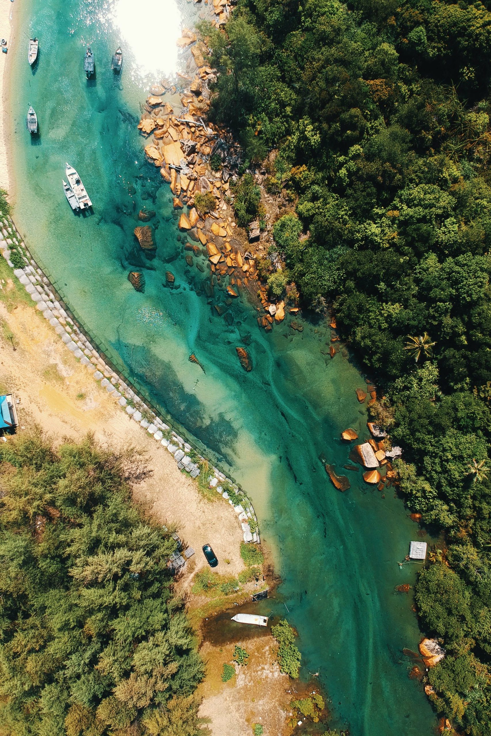 Aerial view of boats on a river. Sand is on one bank and tropical trees on the other.