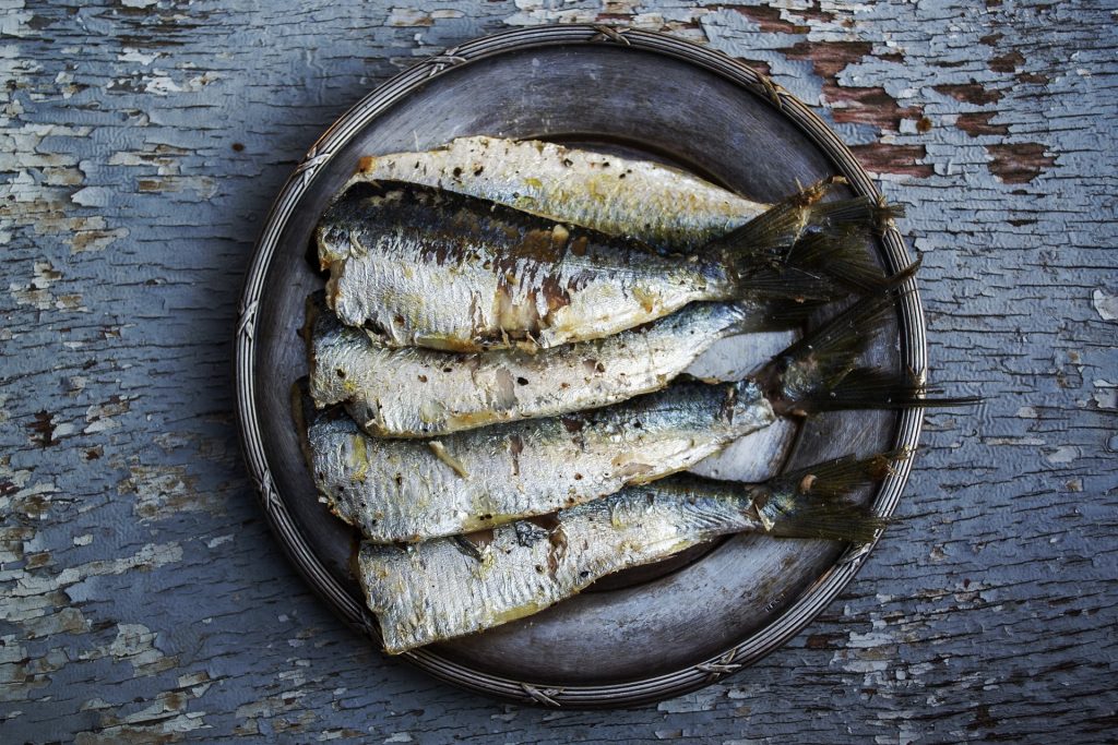 Plat of cooked sardines sit on a rustic wooden table.